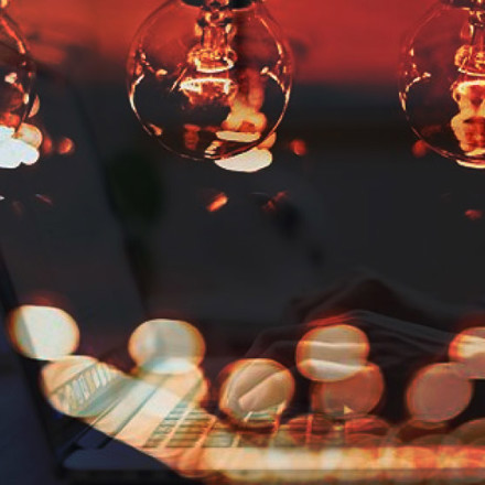 Double exposure image of a woman's hands on a laptop with three light bulbs and lights spots surrounding it.