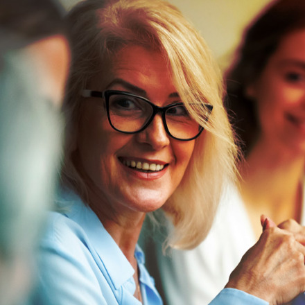 Smiling aged businesswoman looking listening to colleague at team meeting