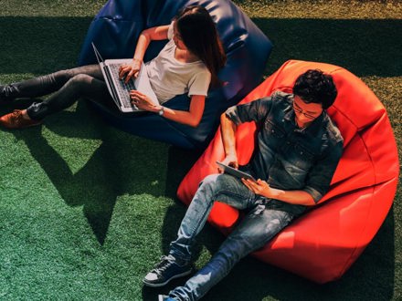 Young Asian couple using laptop notebook and digital tablet together in modern public park, sit on bean bag, top view with copy space on grass.