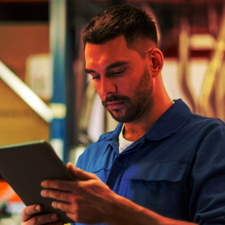 Business man looking down at his tablet in a warehouse setting.