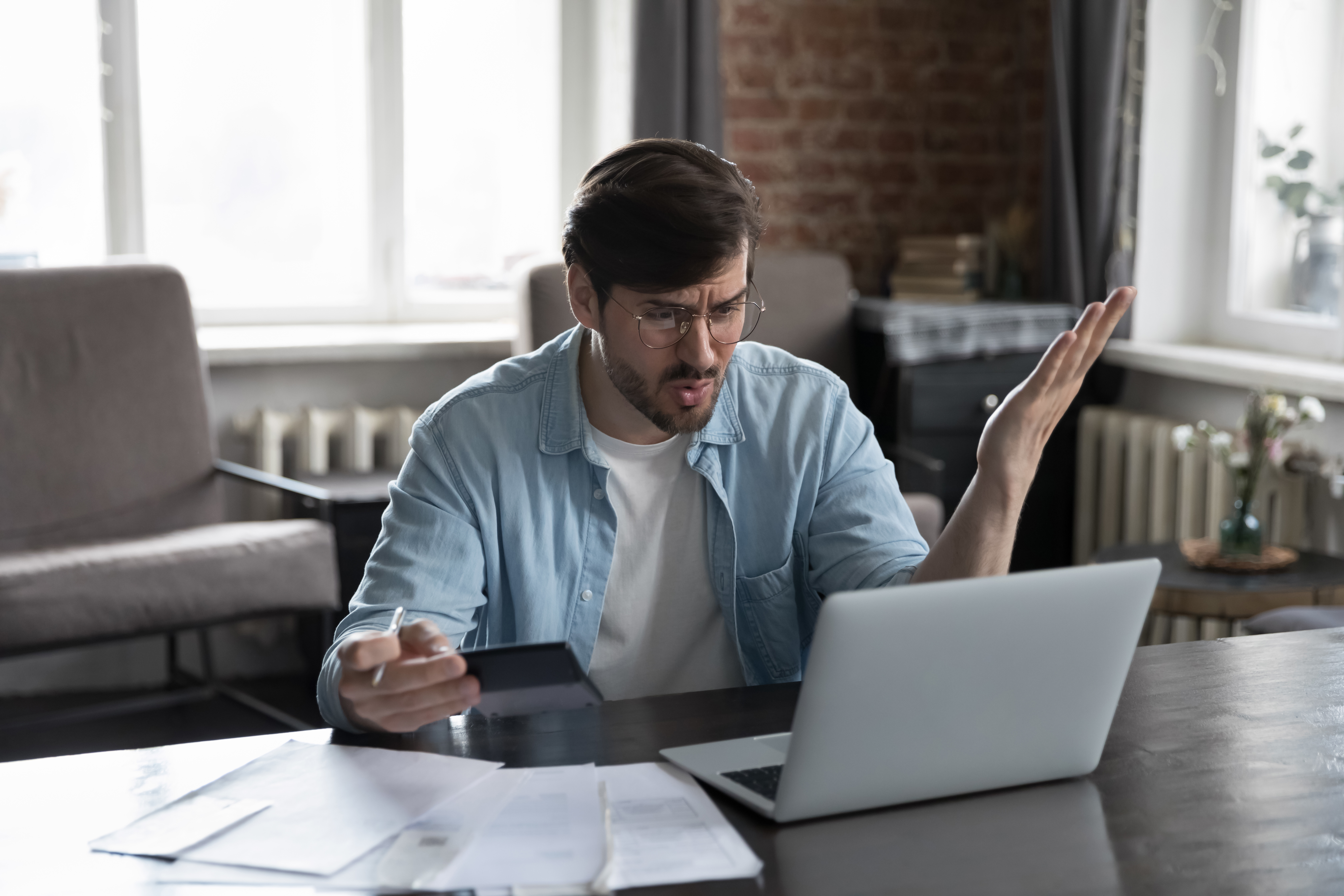 man struggling to read laptop and paper data