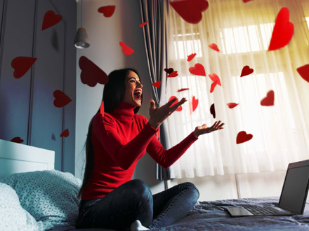 Beautiful, happy, young woman throwing red heart-shapes in the air, sitting on the bed.