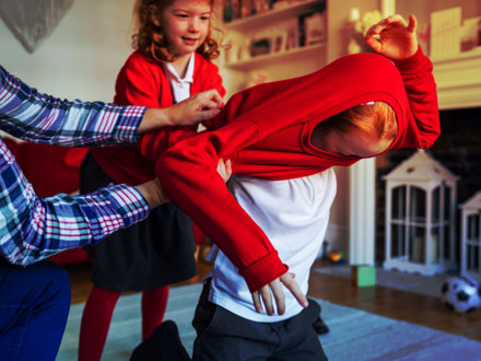 A mother helps her son put on his school uniform ready to start school that day with some help from his sister.