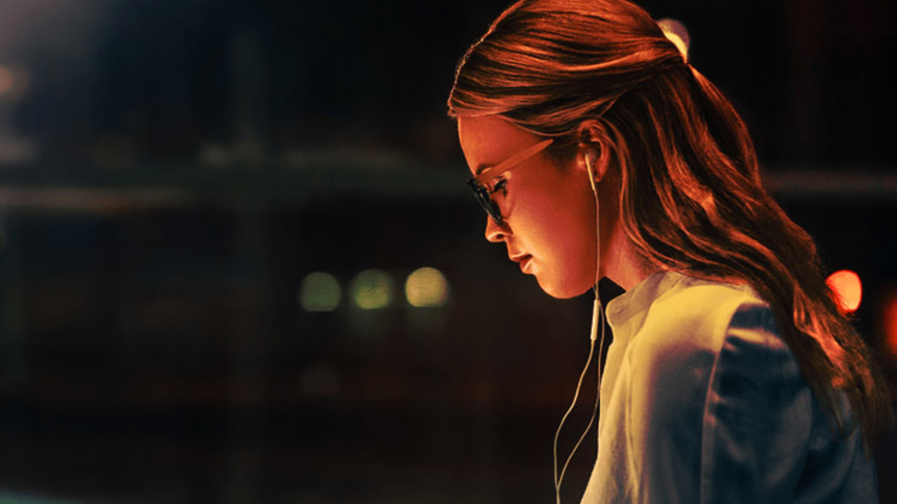 Young woman working late at night on her laptop while wearing earphones.