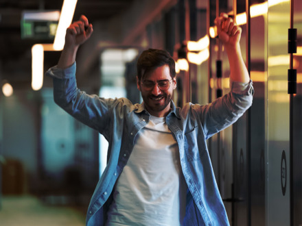 Excited businessmen celebrating career growth dancing in office hallway.