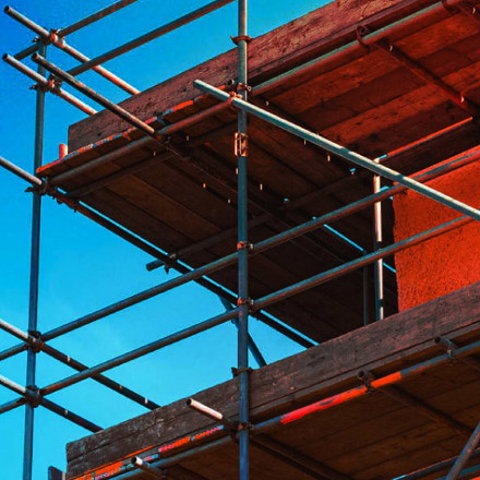 Corner of a home construction with scaffolding against a blue sky.