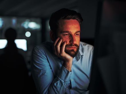 Shot of a young businessman looking tired while working on a computer in an office at night