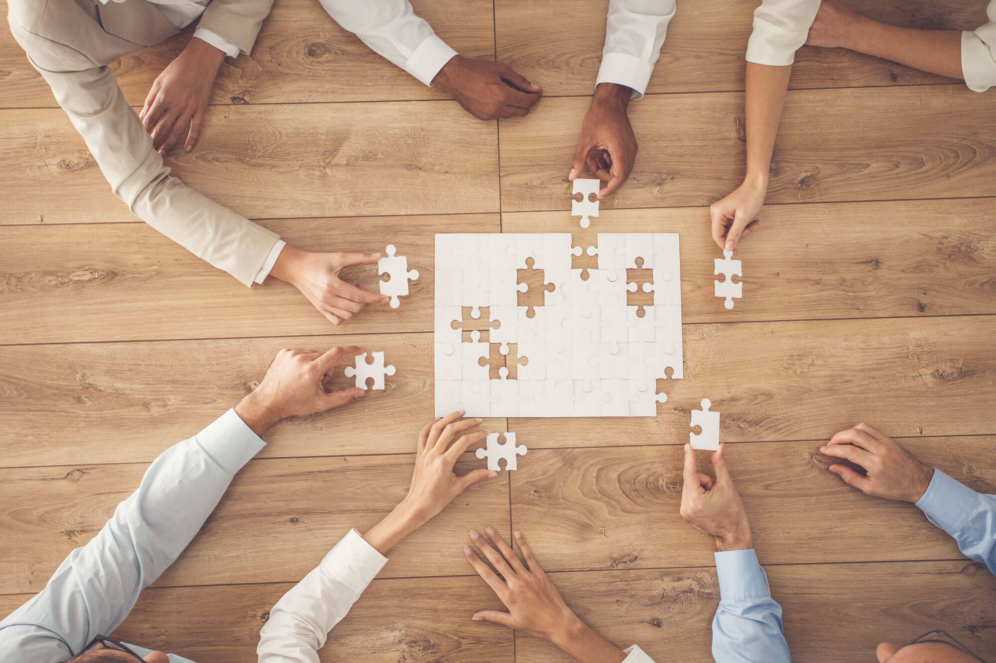 Business people sitting at office desk, putting puzzle pieces together, finding solution, high angle view.