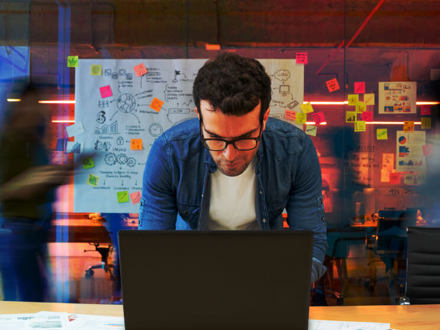 Man working at a creative office using his computer and people moving at the background