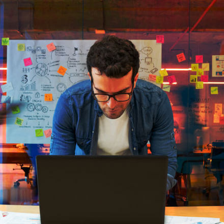 Man working at a creative office using his computer and people moving at the background