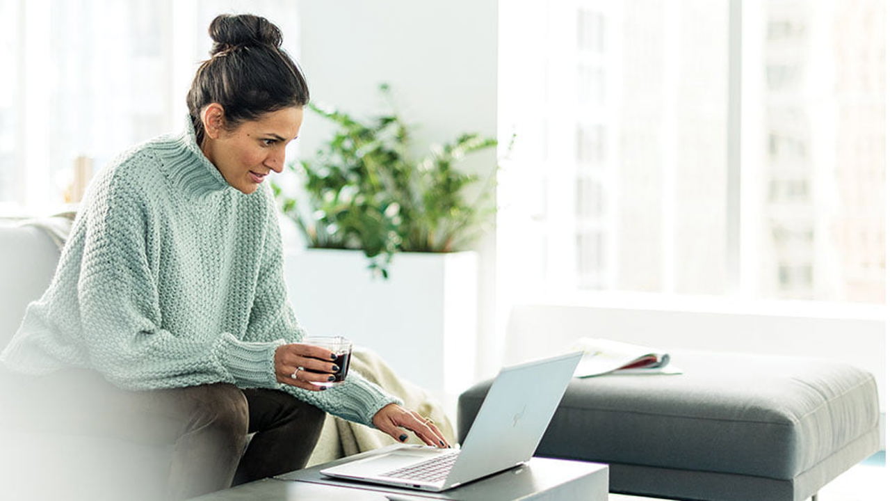 Lady holding a coffee in her right hand while scrolling on her laptop. 