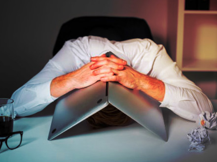 Frustrated man sitting with his head down, and his open laptop straddled over his head. It's a horrible picture. 