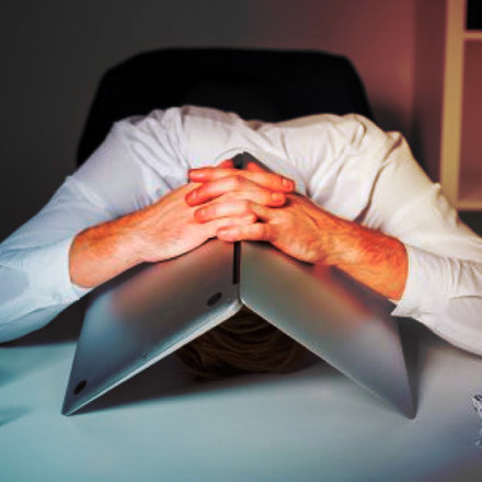 Frustrated man sitting with his head down, and his open laptop straddled over his head. It's a horrible picture. 