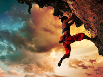 Athletic woman climbing on overhanging cliff rock with sunset sky background.