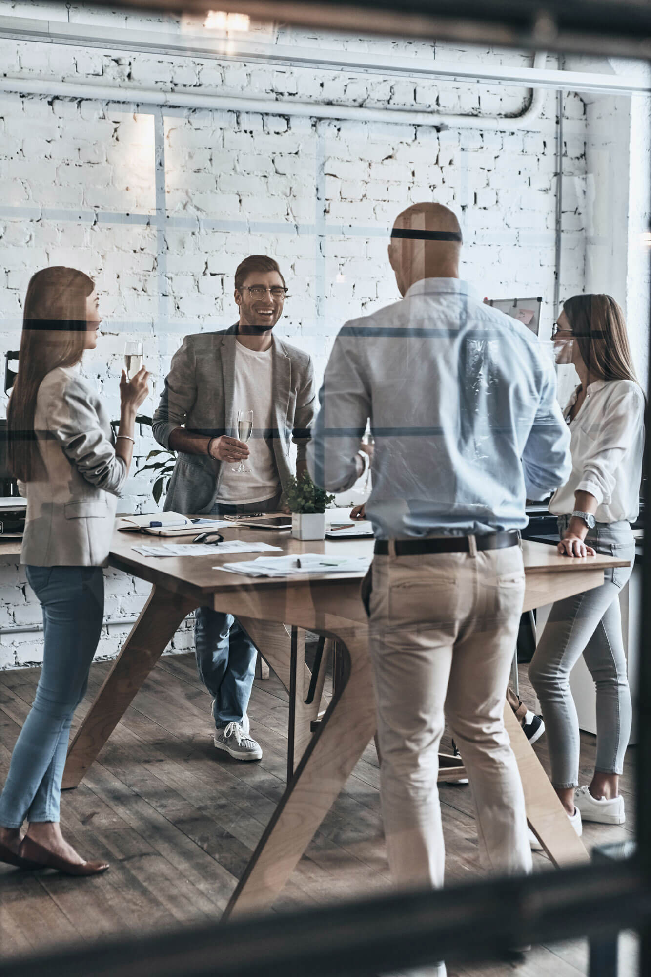 Diverse group of young business people drinking champagne and smiling while standing behind the glass wall in the board room.