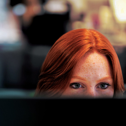 Red haired woman half hidden behind her screen at work. 