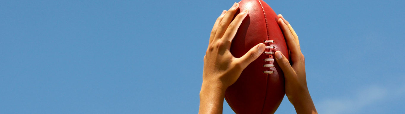 Hands holding Australian football up to the sky