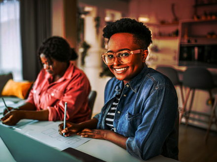 Women working together at home, sitting at same table.