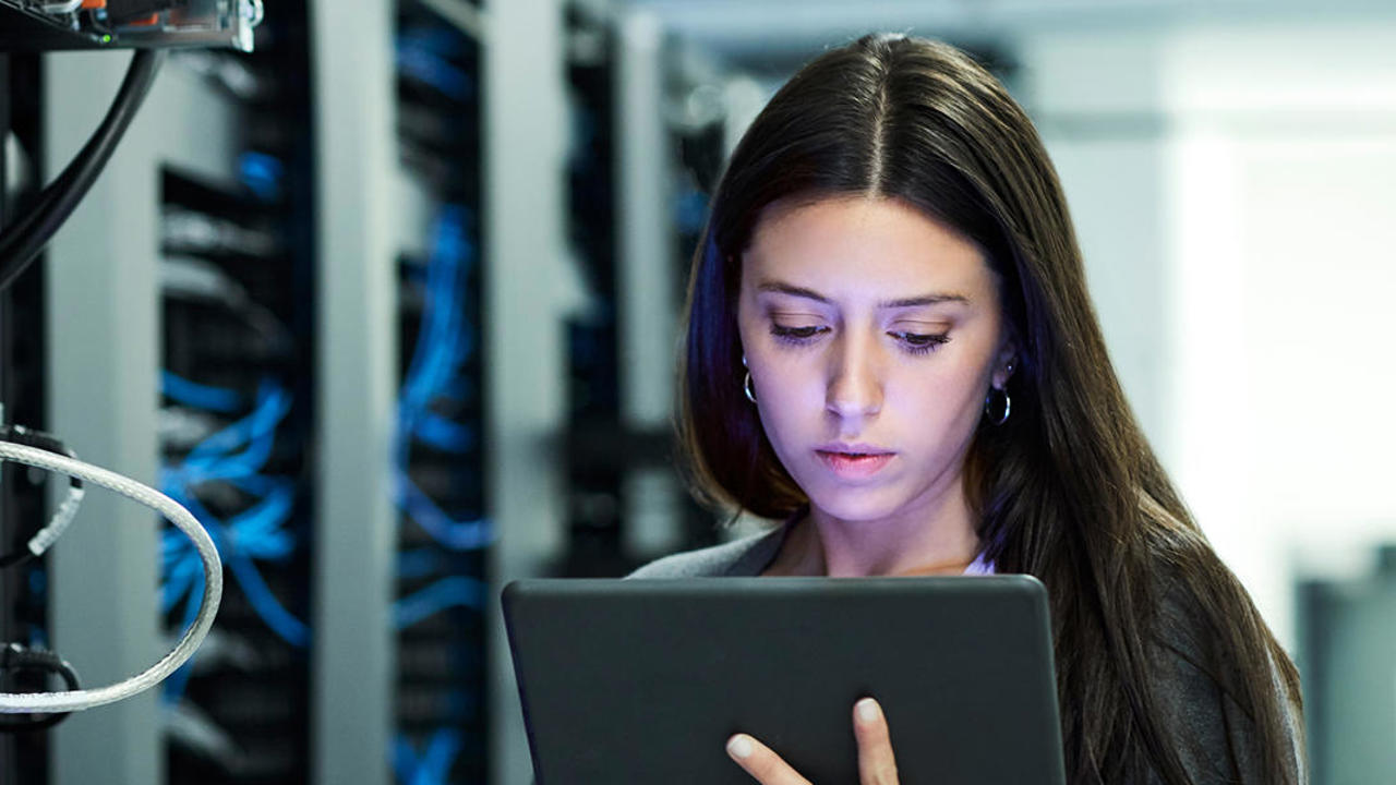 Woman looking at her device while standing next to a data centre. 