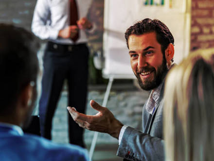 Young happy businessman turning to his colleague and talking to him during a presentation in a board room.