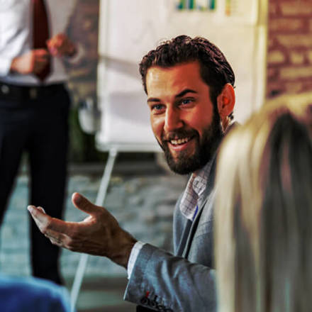 Young happy businessman turning to his colleague and talking to him during a presentation in a board room.