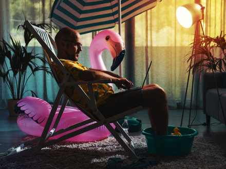 Man spending summer vacations at home alone, he is sitting on the deckchair in the living room and working with a laptop