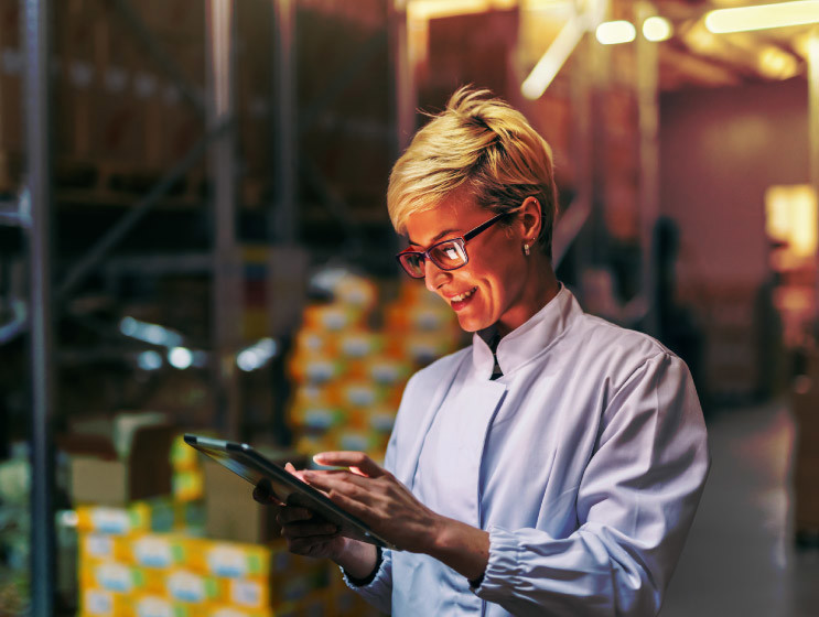 Young Caucasian blonde woman in white uniform using tablet in warehouse.