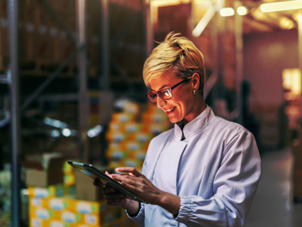 Young Caucasian blonde woman in white uniform using tablet in warehouse.