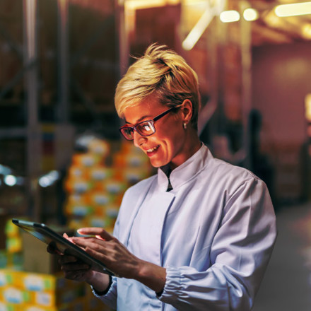 Young Caucasian blonde woman in white uniform using tablet in warehouse.