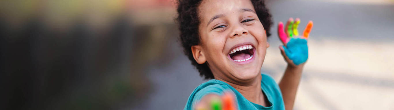 Happy boy with paint of his fingers reaching out to the camera.