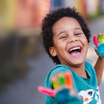 Happy boy with paint of his fingers reaching out to the camera.