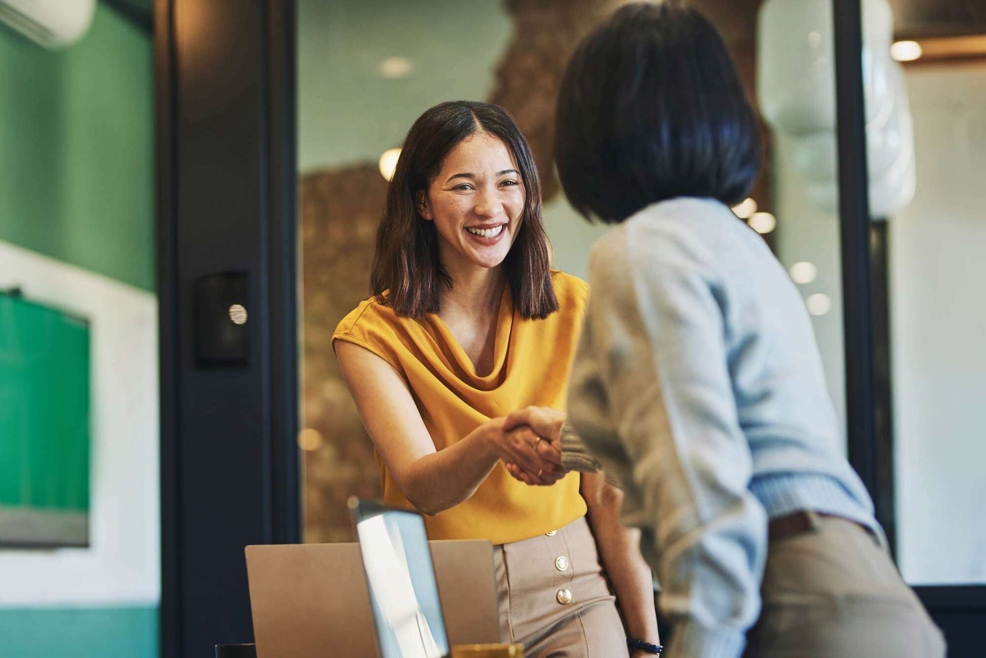 Cheerful businesswomen shaking hands in meeting room.