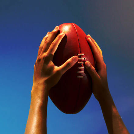 Hands holding Australian football up to the sky