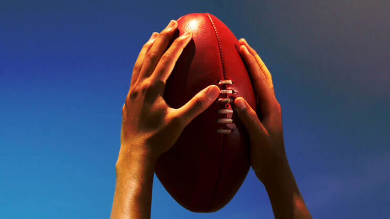 Hands holding Australian football up to the sky