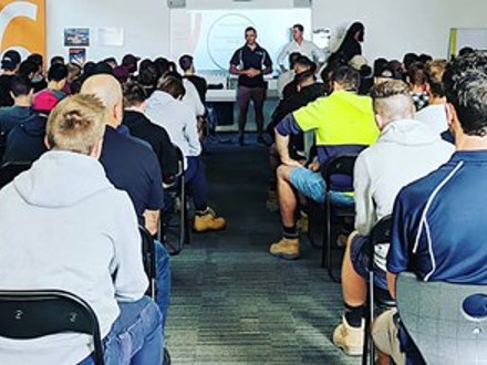 Showing the backs of a large number of people listening to a presentation.