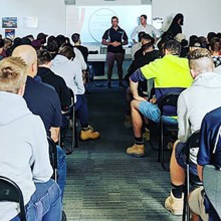 Showing the backs of a large number of people listening to a presentation.