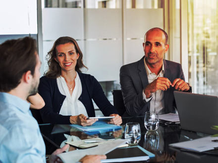 Multiethnic group of business people sitting in annual meeting in conference room. Mature leader with businessmen and businesswomen discussing. Busy partners working together in modern office.