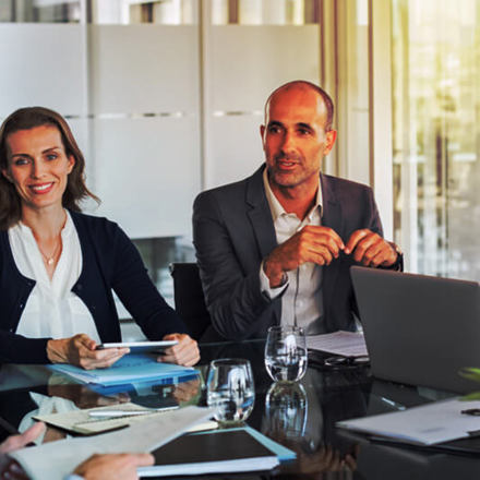 Multiethnic group of business people sitting in annual meeting in conference room. Mature leader with businessmen and businesswomen discussing. Busy partners working together in modern office.