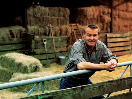 Farmer Leaning on a Gate, With a Barn and Bales of Hay