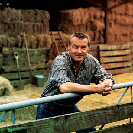 Farmer Leaning on a Gate, With a Barn and Bales of Hay