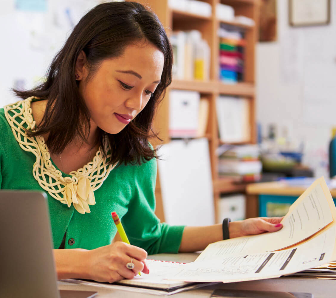 Female Asian teacher at her desk marking students' work