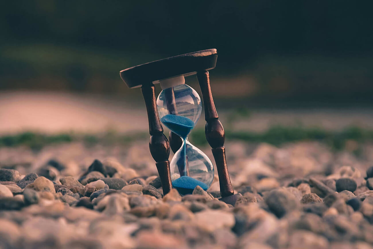 Antique hour glass with blue sand, on pebbles.