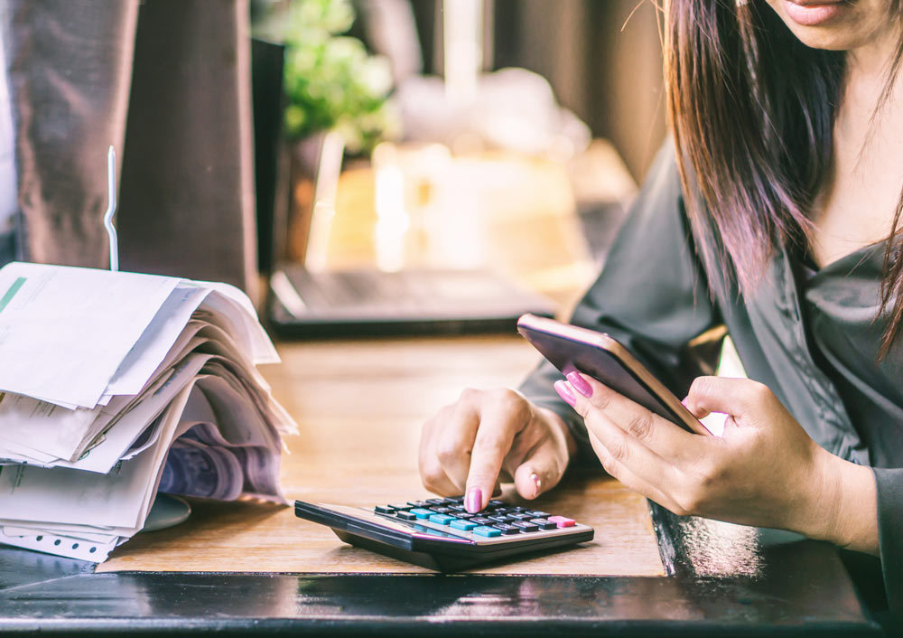 Woman hand calculating her monthly expenses and debt during tax season with financial bills on desk.