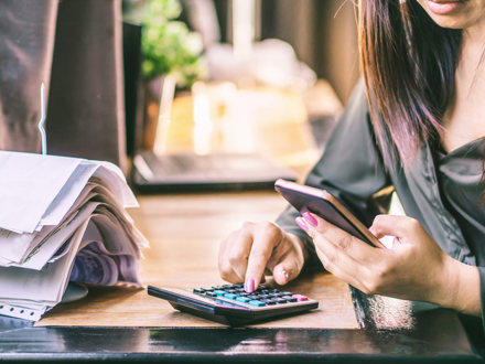 Woman hand calculating her monthly expenses and debt during tax season with financial bills on desk.