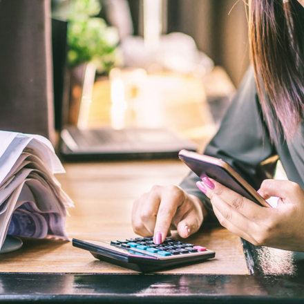 Woman hand calculating her monthly expenses and debt during tax season with financial bills on desk.