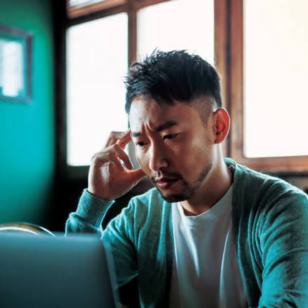 Asian man looking perplexed about his finances on a laptop screen