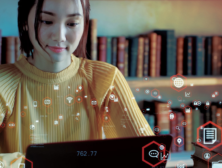 A woman in a yellow sweater works on a laptop in a library. Digital icons float around her, symbolizing connectivity and data. Bookshelves are visible in the background.