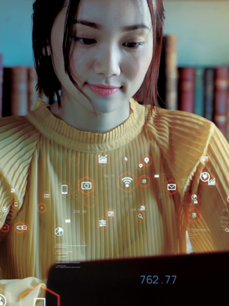 A woman in a yellow sweater works on a laptop in a library. Digital icons float around her, symbolizing connectivity and data. Bookshelves are visible in the background.