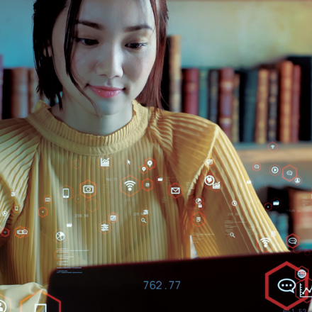 A woman in a yellow sweater works on a laptop in a library. Digital icons float around her, symbolizing connectivity and data. Bookshelves are visible in the background.