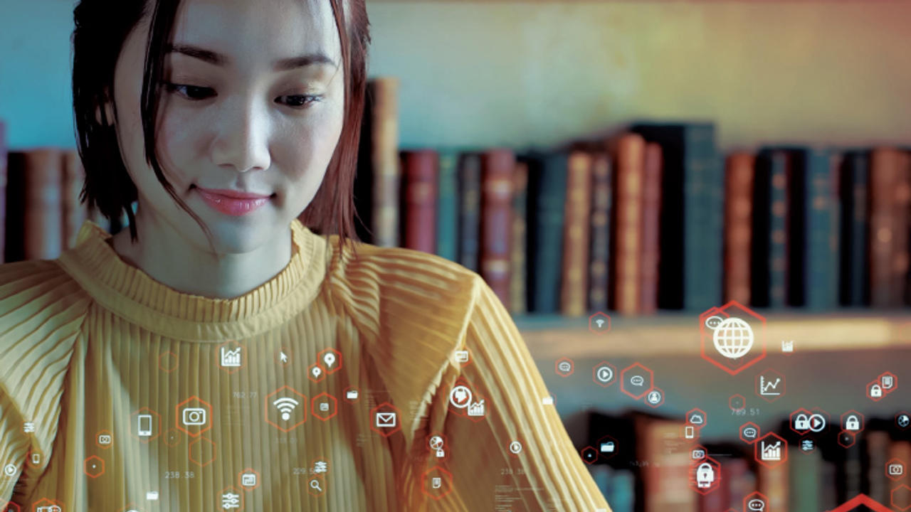 A woman in a yellow sweater works on a laptop in a library. Digital icons float around her, symbolizing connectivity and data. Bookshelves are visible in the background.